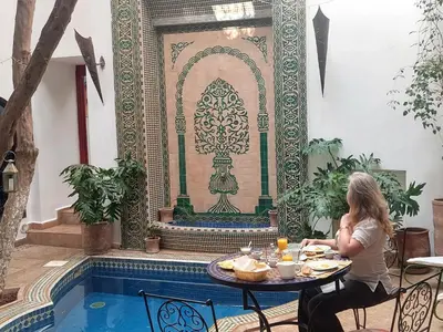 a woman sitting at a table in front of a pool at Riad Alma Mouassine in Marrakech