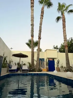 a pool with palm trees in front of a building at Maison d'hôte Darkom Kech in Marrakech