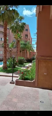 a street with palm trees and a building and a sidewalk at Appart 2 CH lumineux et une piscine pour votre séjour in Marrakech