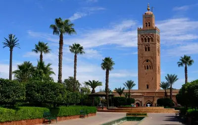 a clock tower with palm trees in front of a building at Appartement 2 chambres à Guéliz avec terrasse et parking in Marrakech