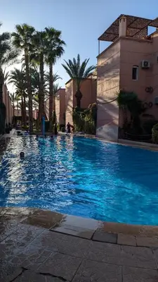 a large blue swimming pool with palm trees and buildings at Rosemary apartment in Marrakech