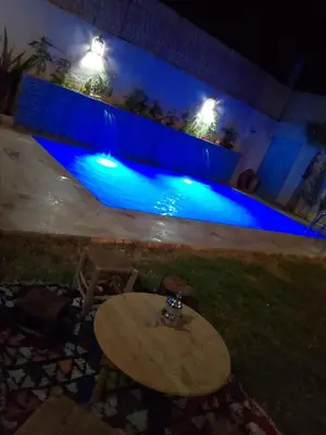 a table in front of a swimming pool at night at Villa El Ilham réservée aux familles in Marrakech