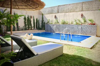 a swimming pool in a yard with a chair and an umbrella at Villa El Ilham réservée aux familles in Marrakech