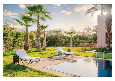 a patio with two chairs and a pool with palm trees at Villa Magnolia avec Jacuzzi, Cuisinière, Piscine in Marrakech