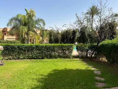 a garden with green grass and trees and a hedge at A Cosy Maison avec un accès direct à la piscine in Marrakech