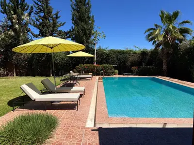 a swimming pool with chairs and umbrellas next to at DAR ENNAGA - Havre de paix, avec piscine chauffée , à 10 minutes de Marrakech in Marrakech