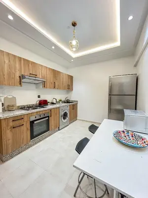 a kitchen with wooden cabinets and a table and a refrigerator at Menara Prestige Duplex 4BR with Pool Access in Marrakech