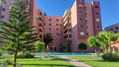 a pink building with a palm tree in front of it at Appartement avec piscine in Marrakech