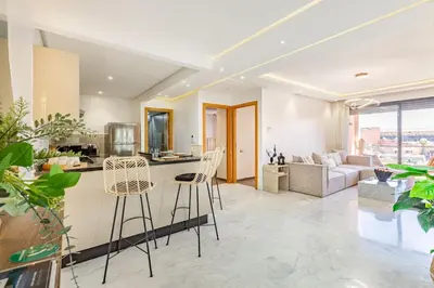 a kitchen and living room with bar stools and a couch at Sakina Appartement Luxe Gueliz in Marrakech
