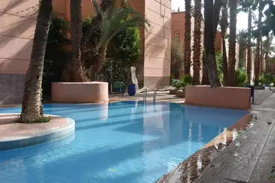 a swimming pool with palm trees and a building at Riad Zaitone 146 in Marrakech