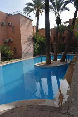a blue swimming pool with palm trees and a building at Riad Zaitone 146 in Marrakech