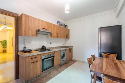 a kitchen with wooden cabinets and a table and a refrigerator at Appartement au coeur de Marrakech à côté de la gare avec piscine in Marrakech
