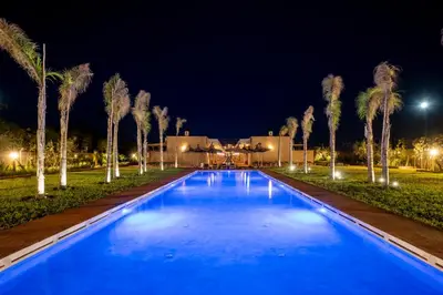 a swimming pool at night with palm trees at Al destino Resort Marrakech in Marrakech