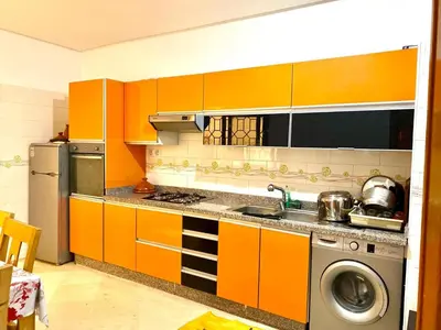 a kitchen with orange cabinets and a washing machine at Magnifique F3 au Riad Arfoud avec piscine in Marrakech