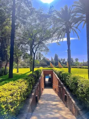 a pathway through a park with palm trees and a tunnel at Apartment with pool and garden in Marrakech