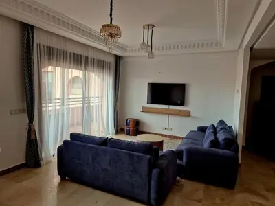 a living room with two blue couches and a tv at Comfortable poolside apartment near city center in Marrakech
