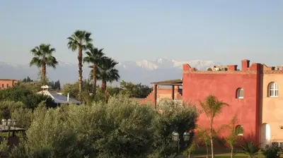 a red building with palm trees and mountains in the background at Villa Yasmine Marrakech in Marrakech