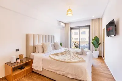 a white bedroom with a large bed and a tv at Appartement Haut de Gamme avec Piscine Privée et Grande Terrasse in Marrakech