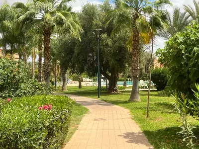a park with palm trees and a sidewalk at L'oasis d'Atlas Golf Resort in Marrakech