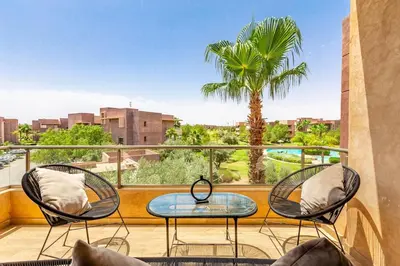 a balcony with two chairs and a table and a palm tree at Opulent 3BR apartment, pool view in Marrakech
