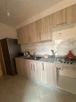 a kitchen with wooden cabinets and a black refrigerator at Appartement 2 chambre cosy in Marrakech