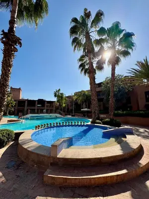 a swimming pool with palm trees in a resort at Oasis de Charme au coeur de la zone touristique in Marrakech