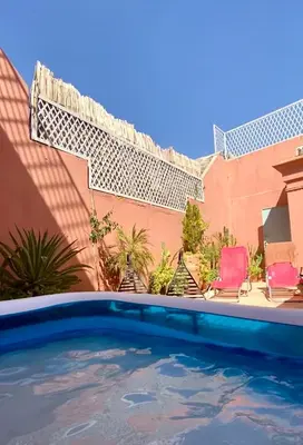 a swimming pool in front of a house with two chairs at Riad Sylvia in Marrakech