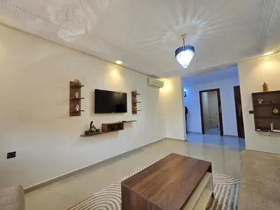 a living room with a table and a tv on a wall at Appartement de luxe, Marrakech Menara in Marrakech