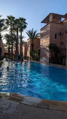 a large blue swimming pool with palm trees and a building at Atelier des Reeves in Marrakech
