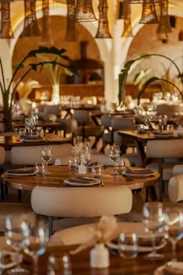 a restaurant with wooden tables and chairs with wine glasses at NOMMOS Beach RESORT & POOL CLUB in Marrakech