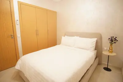 a bedroom with a white bed with a wooden cabinet at New cozy 2 bedroom apartment with 3 ACs close to airport and center in Marrakech