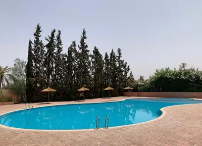 a large blue swimming pool with umbrellas and trees at Élégance & fraîcheur Appart avec piscine in Marrakech