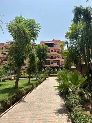 a walkway in a park with trees and a building at Apparemment première village in Marrakech