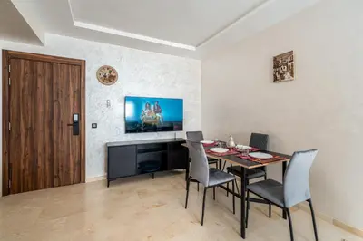 a dining room with a table and chairs and a television at Cocon Sable piscine et parking in Marrakech