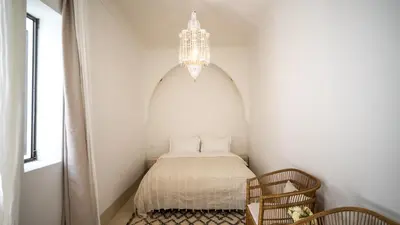 a bed in a white room with a chandelier at Riad Dar Mimi in Marrakech