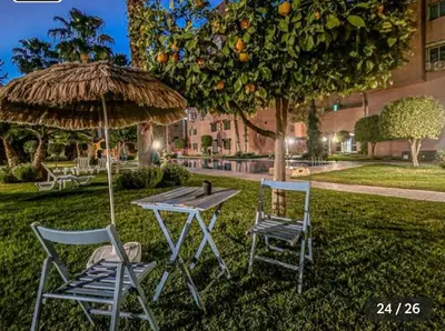 two chairs and a table and an umbrella in the grass at Appartement Marrakech in Marrakech
