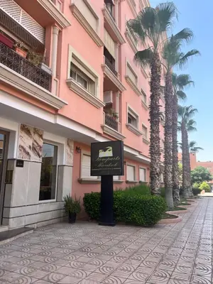 a sign in front of a pink building with palm trees at Prestigieux Appart hivernage in Marrakech