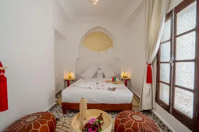 a bedroom with a bed and a table and windows at Riad Fleur De Sable in Marrakech