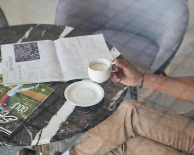 a person holding a cup of coffee on a table with a newspaper at Pickalbatros SUNGO Club - All Inclusive in Marrakech