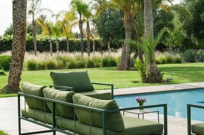 a patio with two chairs and a table next to a pool at Adnaa - Modern Villa with 2 pools, sauna, hammam, tennis court & home cinema in Douar Caïd Layadi