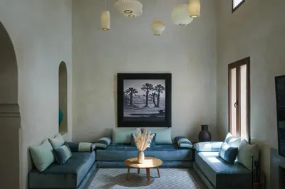 a living room with a blue couch and palm trees at Adnaa - Modern Villa with 2 pools, sauna, hammam, tennis court & home cinema in Douar Caïd Layadi