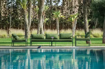 a green couch sitting next to a swimming pool at Adnaa - Modern Villa with 2 pools, sauna, hammam, tennis court & home cinema in Douar Caïd Layadi