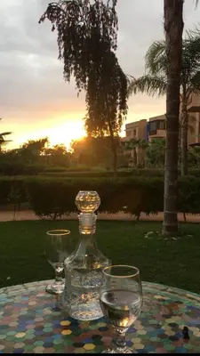 two wine glasses and a bottle on a table with the sunset at Almaz appartement in Marrakech