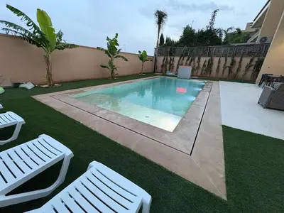 a swimming pool with two white chairs next to a house at Villa del Sur 5 min du centre in Marrakech