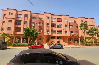a red car parked in front of a large building at Bright 2-BR - Balcony & Parking - Fast Wi-Fi - Near Route de Casa in Marrakech