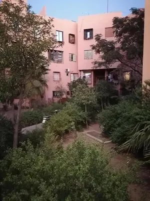 a pink building with trees and bushes in front of it at Menara Airport Appartement - 10 Min Walk in Marrakech