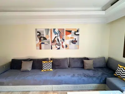 a blue couch in a living room with paintings on the wall at Appartement de Luxe avec Piscine et Jacuzzi Marrakech in Marrakech