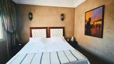 a bedroom with a bed with white sheets and a painting at Bloom Hivernage Deluxe - 2 Chambres - Le Soleil en Mars - Petit déjeuner et Services de chambres inclus - A 10mn des sites - Balcon végétal in Marrakech
