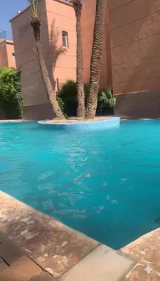 a blue swimming pool with palm trees next to a building at Riad Nahara in Marrakech