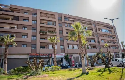 a large building with palm trees in front of it at Cosy Appartement de Luxe F3 Menara Garden Hivernage Marrakech avec piscine in Marrakech